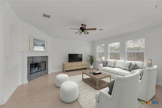 living area featuring a tiled fireplace, visible vents, ceiling fan, and wood finished floors