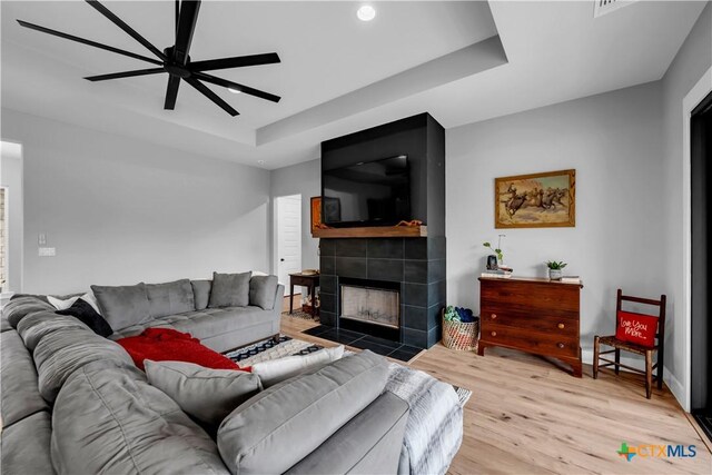 123 Wandering Oak Cir, Burnet, TX 78611 - living room featuring a tiled fireplace, light wood-style floors, a raised ceiling, and ceiling fan
