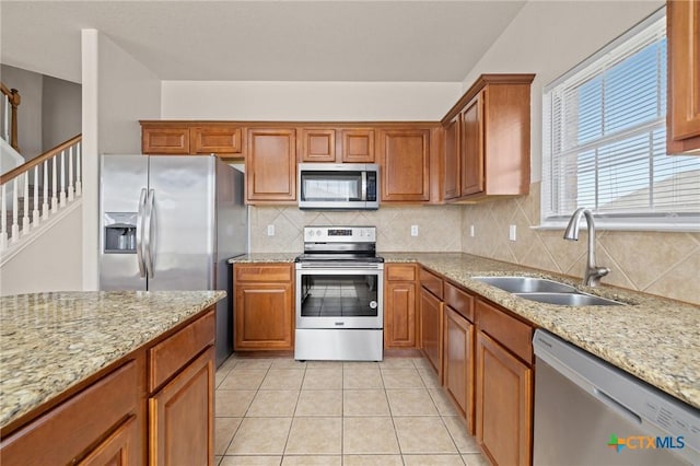 kitchen with brown cabinets, stainless steel appliances, decorative backsplash, light tile patterned flooring, and a sink