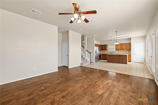 unfurnished living room featuring stairs, light wood-type flooring, visible vents, and baseboards