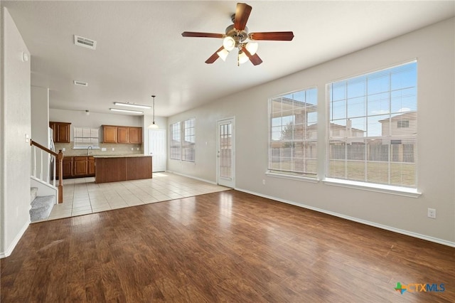 unfurnished living room with ceiling fan, stairway, visible vents, and light wood-style floors