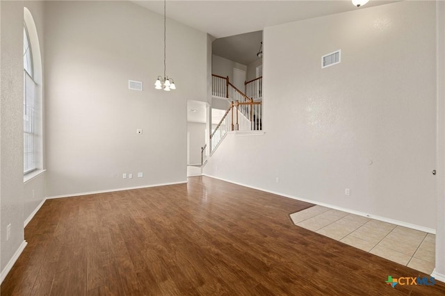 unfurnished living room with stairs, visible vents, a chandelier, and wood finished floors