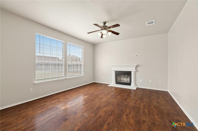 unfurnished living room featuring baseboards, visible vents, a ceiling fan, a glass covered fireplace, and dark wood-type flooring