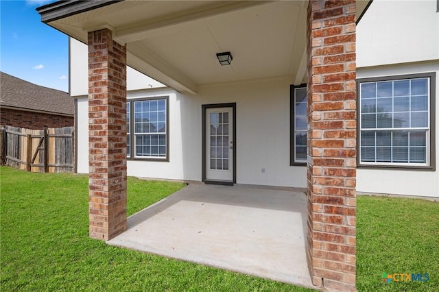 doorway to property with a yard, brick siding, fence, and stucco siding