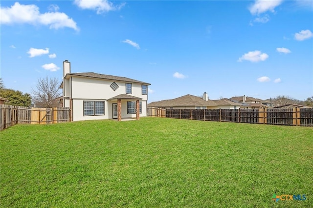 back of property with stucco siding, a fenced backyard, a chimney, and a yard