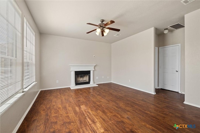 unfurnished living room featuring wood finished floors, a wealth of natural light, a glass covered fireplace, and visible vents