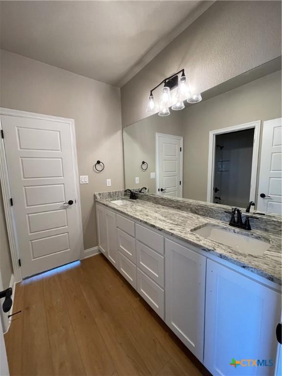 bathroom featuring double vanity, a sink, baseboards, and wood finished floors