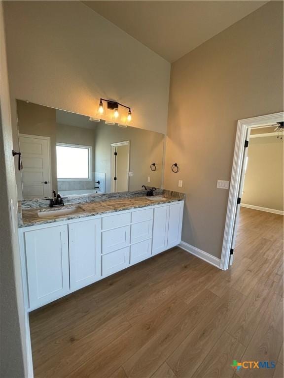 bathroom featuring lofted ceiling, wood finished floors, a sink, baseboards, and double vanity