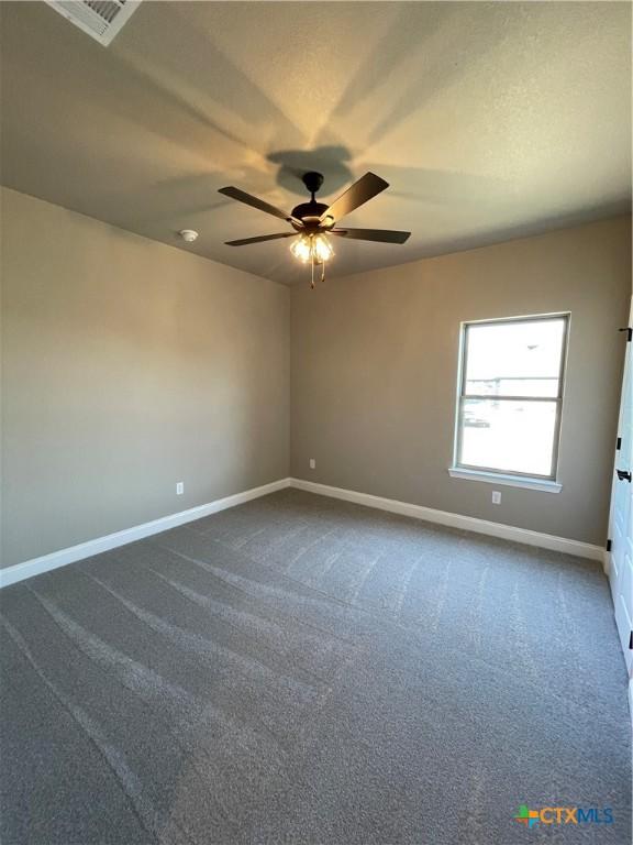 spare room featuring a textured ceiling, dark carpet, a ceiling fan, and baseboards