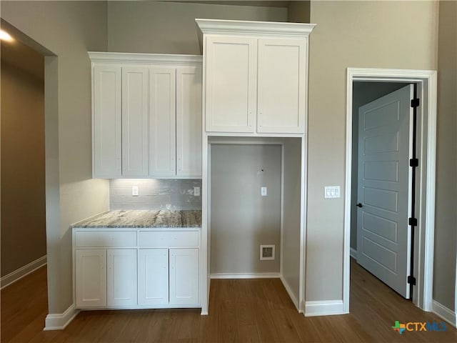 kitchen featuring light stone countertops, backsplash, white cabinets, wood finished floors, and baseboards