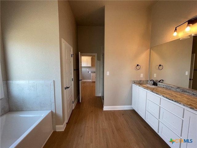 full bathroom featuring a garden tub, vanity, baseboards, and wood finished floors