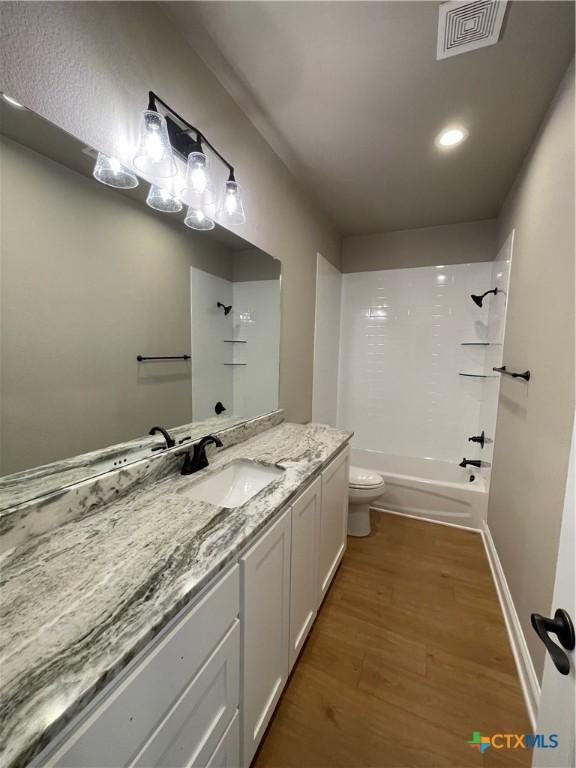 bathroom with shower / bath combination, visible vents, toilet, vanity, and wood finished floors