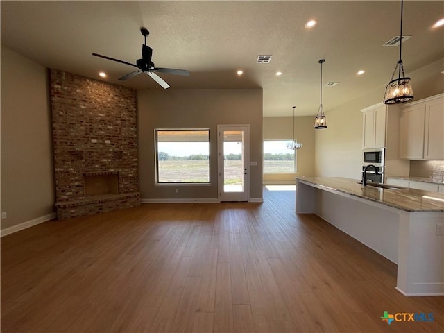 kitchen featuring stainless steel microwave, visible vents, open floor plan, a sink, and light stone countertops