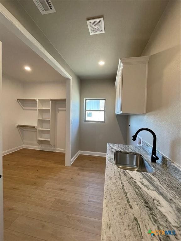 kitchen featuring a sink, visible vents, baseboards, white cabinetry, and light wood finished floors