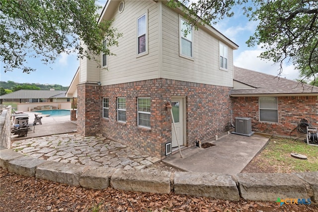 back of house with brick siding, a shingled roof, a patio, cooling unit, and an outdoor pool