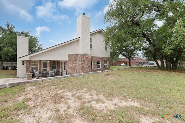 back of house with a chimney, brick siding, fence, a patio area, and a lawn