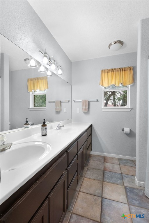 bathroom featuring baseboards, toilet, double vanity, and a sink