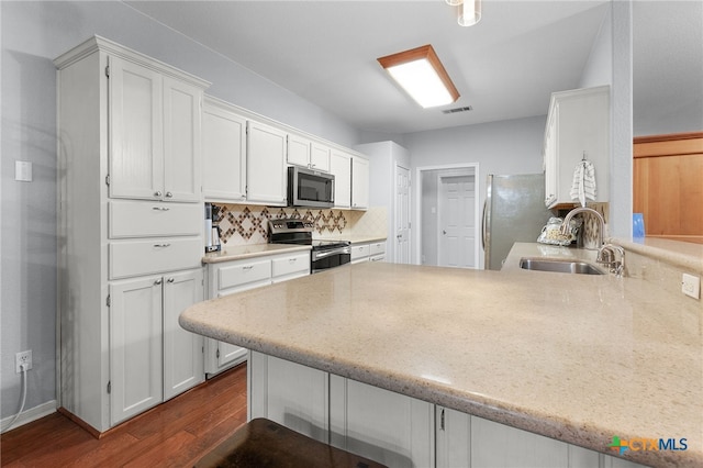 kitchen featuring dark wood-style floors, a sink, a peninsula, white cabinetry, and appliances with stainless steel finishes