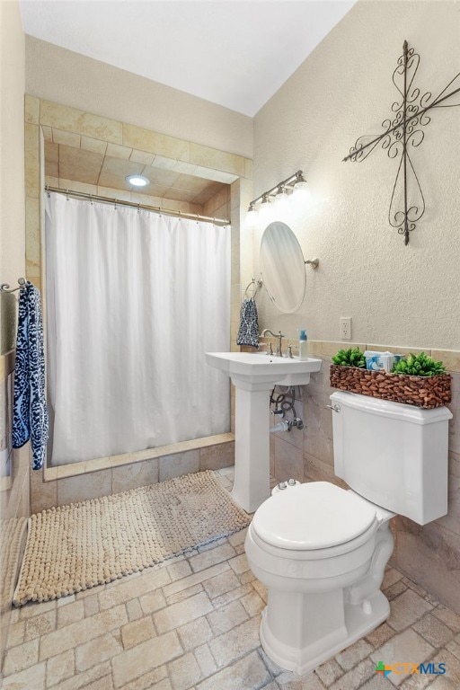 bathroom with curtained shower, toilet, a textured wall, and tile walls