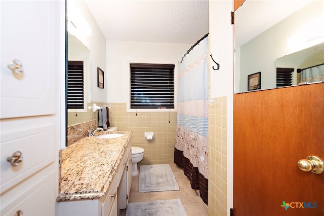 bathroom with tile walls, vanity, tile patterned flooring, curtained shower, and toilet