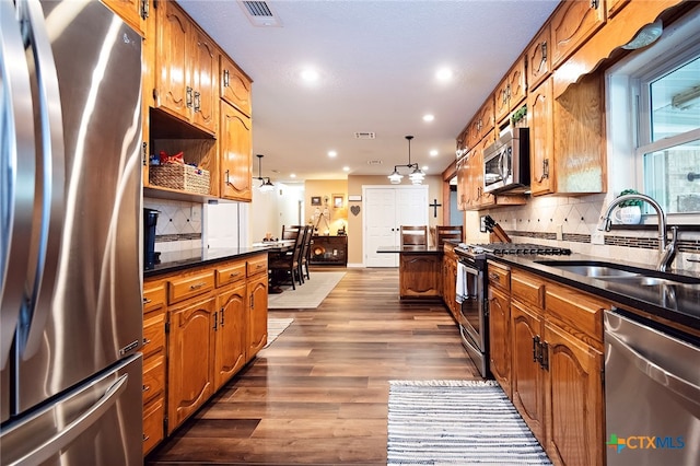 kitchen featuring stainless steel appliances, dark hardwood / wood-style floors, pendant lighting, decorative backsplash, and sink