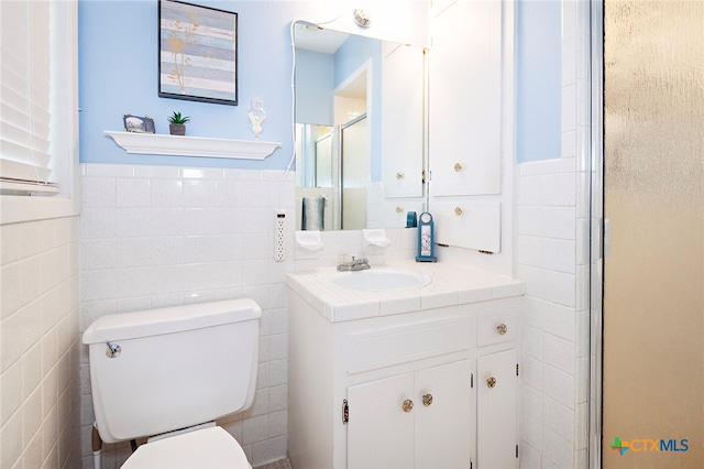 bathroom with vanity, toilet, an enclosed shower, and tile walls