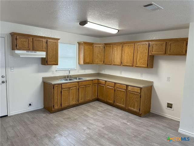 1718 S 15th St, Temple, TX 76504 - kitchen with brown cabinetry, light wood-style floors, a textured ceiling, and under cabinet range hood