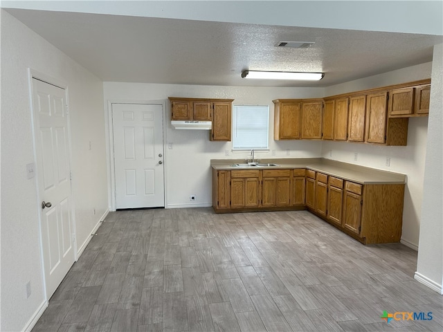 1718 S 15th St, Temple, TX 76504 - kitchen featuring brown cabinets, light wood-type flooring, under cabinet range hood, and light countertops