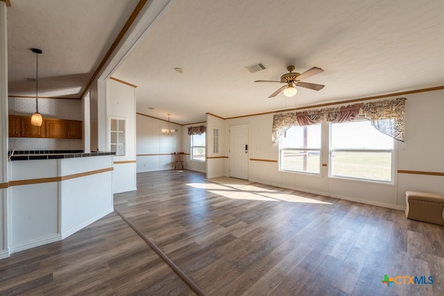 unfurnished living room with a textured ceiling, ceiling fan with notable chandelier, crown molding, and dark wood-type flooring