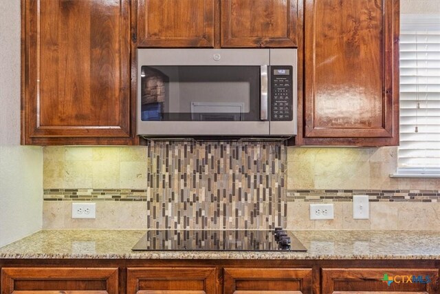 5907 Verde Dr, Killeen, TX 76549 - kitchen featuring stainless steel microwave, black electric stovetop, backsplash, and light stone counters