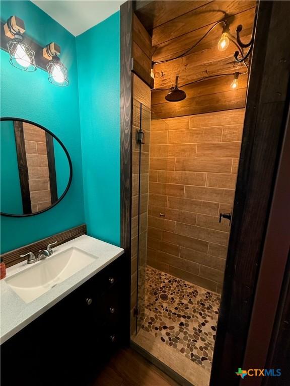 bathroom with a tile shower, vanity, and wood finished floors