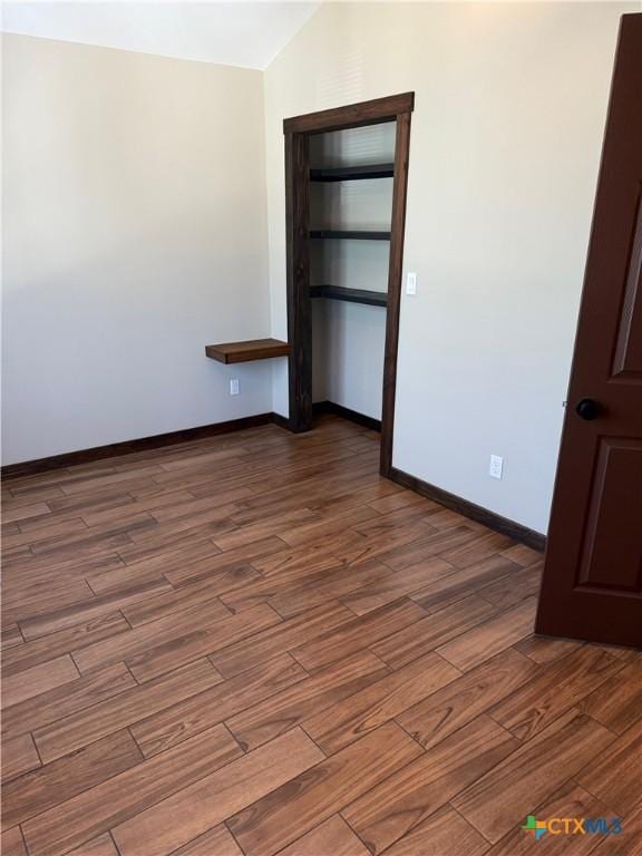 unfurnished bedroom with wood finished floors, lofted ceiling, baseboards, and a closet