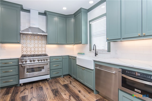 kitchen featuring wall chimney range hood, appliances with stainless steel finishes, dark hardwood / wood-style floors, sink, and decorative backsplash