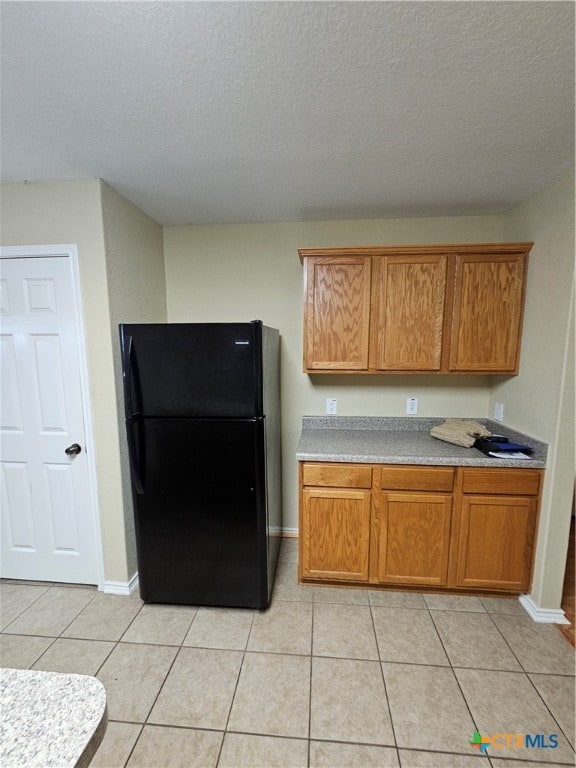 kitchen with light tile patterned floors, a textured ceiling, and black fridge