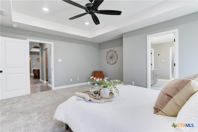 bedroom featuring light carpet, ensuite bathroom, ceiling fan, and a tray ceiling