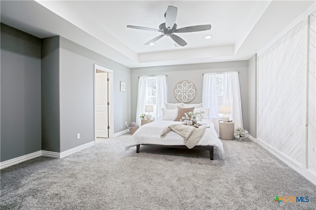 carpeted bedroom featuring multiple windows, a tray ceiling, and ceiling fan