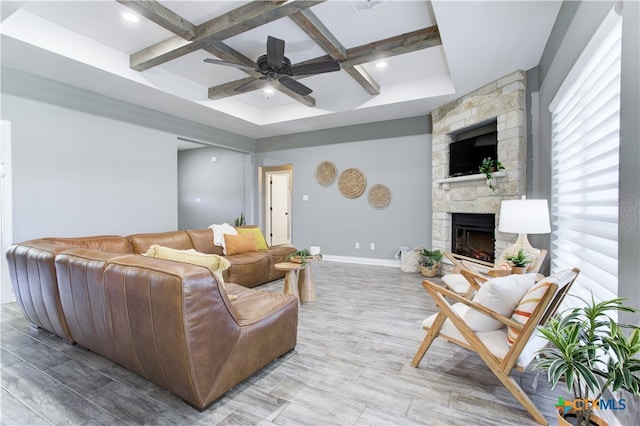 living room with coffered ceiling, a stone fireplace, light hardwood / wood-style flooring, ceiling fan, and beamed ceiling