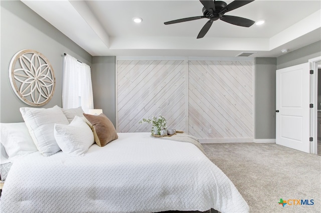 carpeted bedroom with a tray ceiling, ceiling fan, and wooden walls