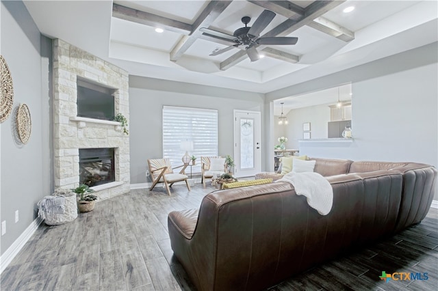 living room with ceiling fan, coffered ceiling, a stone fireplace, beamed ceiling, and wood-type flooring