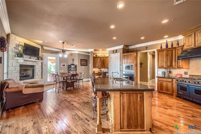 547 Powder Rdg, Luling, TX 78648 - kitchen featuring appliances with stainless steel finishes, under cabinet range hood, crown molding, open floor plan, and light wood finished floors