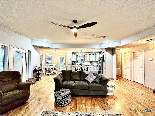 living room featuring ceiling fan, light wood-type flooring, and a textured ceiling