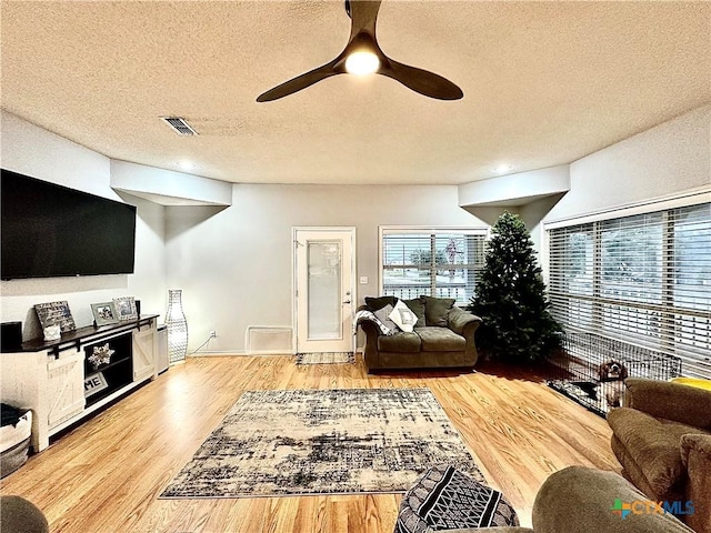 living room featuring ceiling fan, light hardwood / wood-style floors, and a textured ceiling