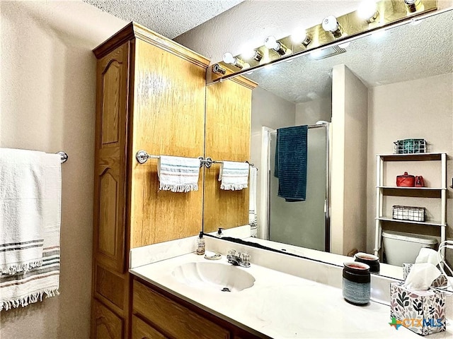 bathroom featuring vanity, a textured ceiling, toilet, and a shower with shower door