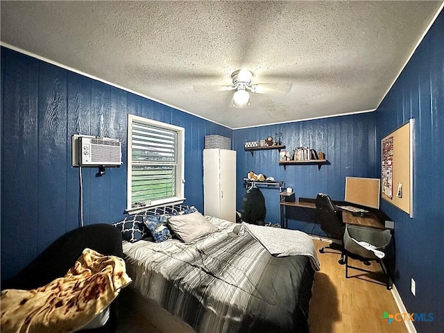 bedroom with an AC wall unit, wooden walls, hardwood / wood-style flooring, ceiling fan, and a textured ceiling