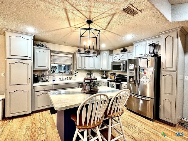 kitchen with sink, hanging light fixtures, light hardwood / wood-style flooring, a kitchen island, and appliances with stainless steel finishes