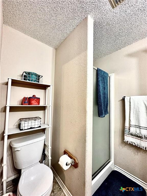 bathroom with toilet, a shower with shower door, and a textured ceiling