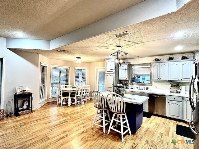 kitchen featuring stainless steel dishwasher, light hardwood / wood-style floors, decorative light fixtures, decorative backsplash, and a kitchen island