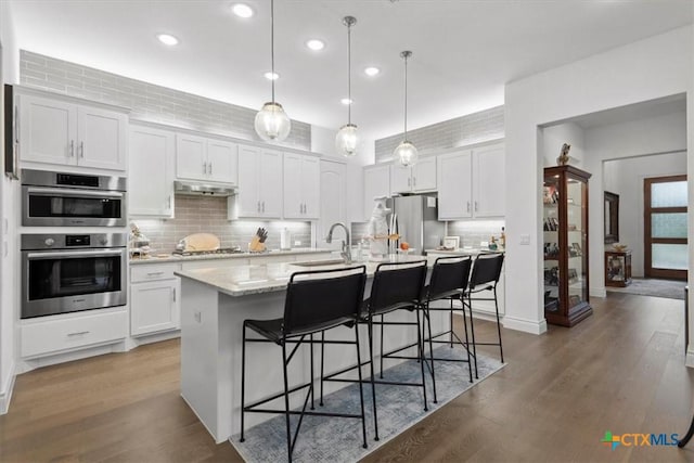 119 Rivalto Dr, Horseshoe Bay, TX 78657 - kitchen with stainless steel appliances, under cabinet range hood, decorative backsplash, white cabinets, and a kitchen breakfast bar