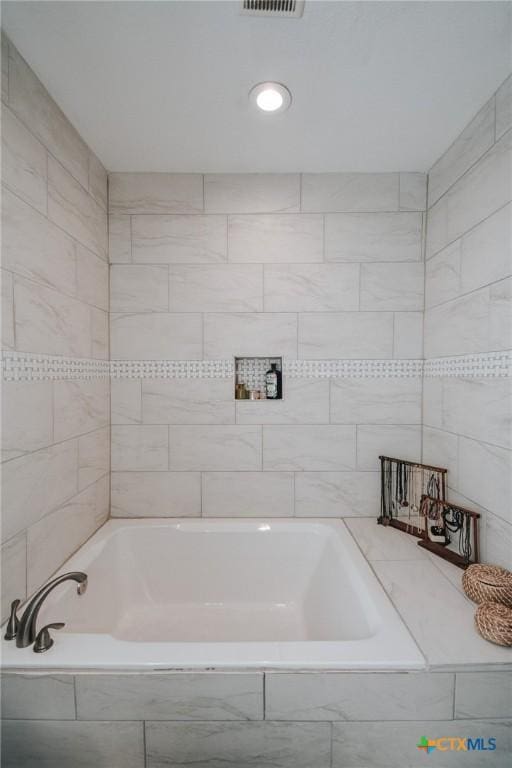 bathroom with tiled tub and visible vents