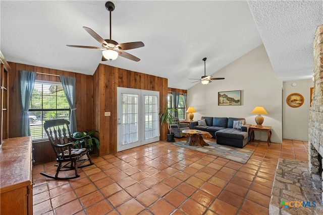 tiled living room featuring ceiling fan, a textured ceiling, high vaulted ceiling, a fireplace, and wooden walls